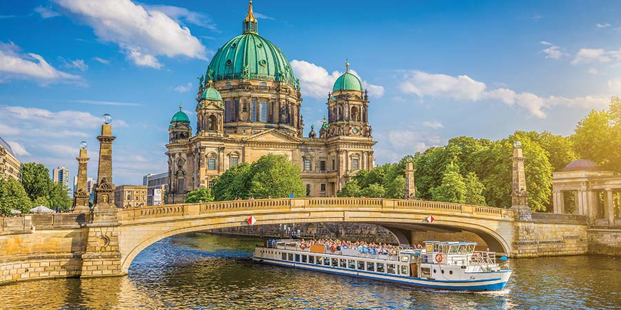 A tour boat passes under the bridge in front of the Berlin Cathedral on a sunny day.