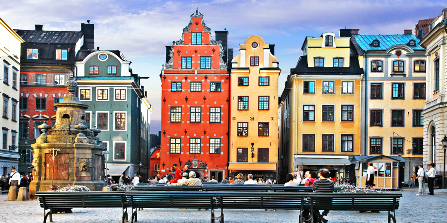 Tourists enjoy the traditional architecture of Stockholm’s old town buildings. The houses are pale yellow and bright red with many windows and ornate roof designs.  