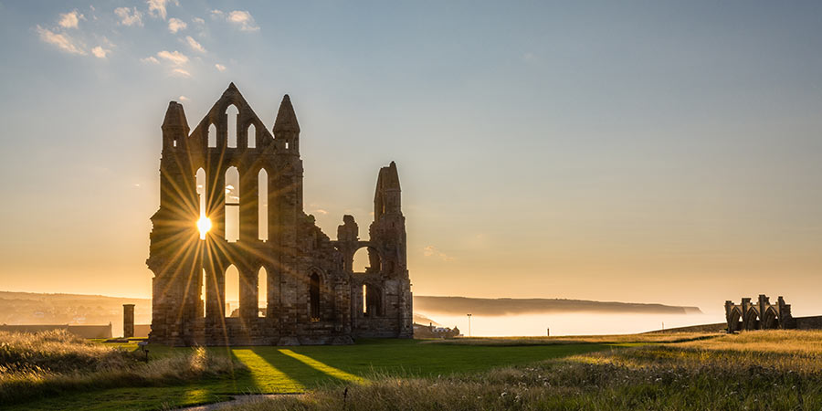 Sun shines through an old Abbey at sunset, behind is mist covering the sea. 